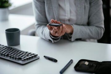 Close up of woman using digital glucometer in office. Young woman checking blood sugar level	