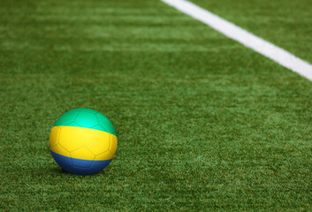 Gabon flag on ball at soccer field background. National football theme on green grass. Sports competition concept. © sezerozger