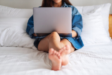 A beautiful asian woman using and working on laptop computer while lying on a white cozy bed at home
