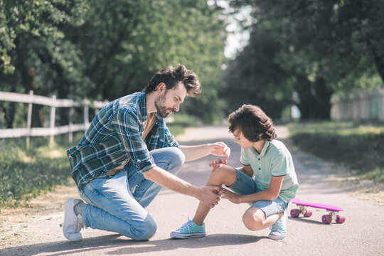 Man in a checkered shirt examining his sons injured knee and looking serious