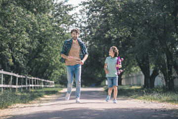 Dark-haired boy with a skateboard and his father running in the park