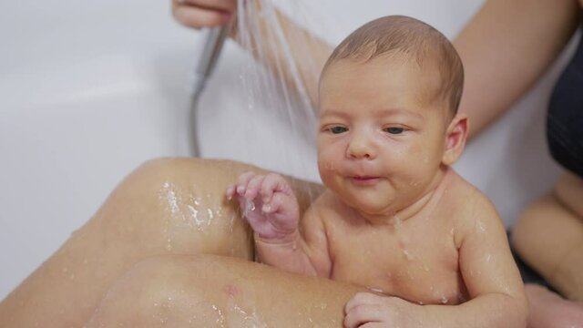 Newborn baby girl is taking bath in bathroom at home. Hygiene and health care for newborn baby.