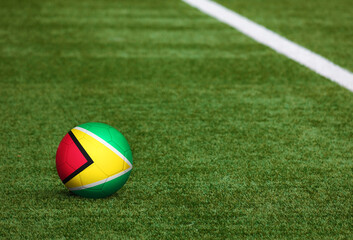 Fototapeta na wymiar Guyana flag on ball at soccer field background. National football theme on green grass. Sports competition concept.