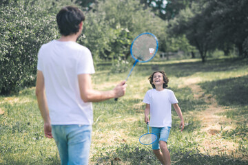 Dark-haired boy and his father playing badminton in the park