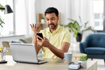 technology, remote job and failure concept - angry indian man with smartphone and laptop computer at home office