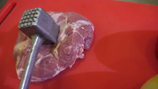 Slab of raw beaf is softened with a metallic pounder in a restaurant kitchen in slo-mo