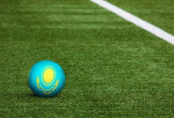 Kazakhstan flag on ball at soccer field background. National football theme on green grass. Sports competition concept.