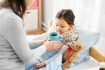 family, health and people concept - mother giving mug with hot tea to sick little daughter lying in...