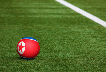 Fototapeta na wymiar North Korea flag on ball at soccer field background. National football theme on green grass. Sports competition concept.