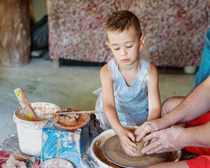 Potter teaches a little kid how make clay pot. Hands working on pottery wheel.