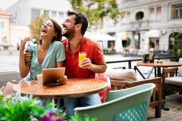 Embracing couple using digital tablet, smiling and talking in cafe