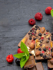 Chocolate bars, various ripe berries and mint leaves lie on a black slate background.