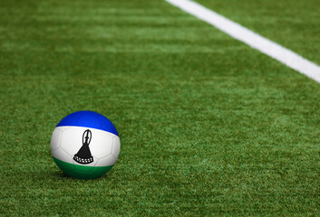 Lesotho flag on ball at soccer field background. National football theme on green grass. Sports competition concept.