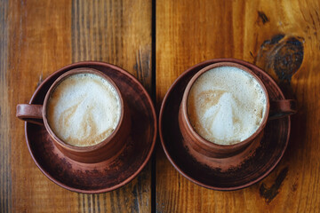 Two retro cups of coffee. Latte in dark brown clay mugs on wooden table.