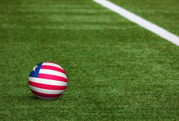 Liberia flag on ball at soccer field background. National football theme on green grass. Sports competition concept.
