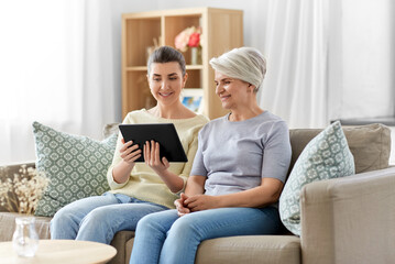 family, generation and technology concept - happy smiling senior mother and adult daughter with tablet pc computer at home