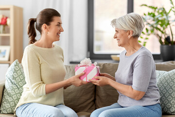 family, mother's day and birthday concept - happy smiling adult daughter giving present to her...