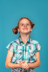Emotional portrait of a little funny naughty girl with red hair  against  blue background