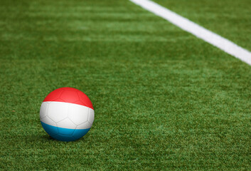 Fototapeta na wymiar Luxembourg flag on ball at soccer field background. National football theme on green grass. Sports competition concept.