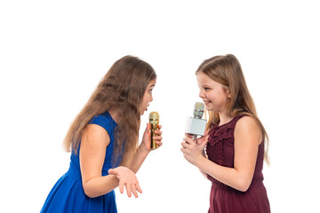 Two young girls brunette and blonde sing songs while holding microphones in their hands, isolated