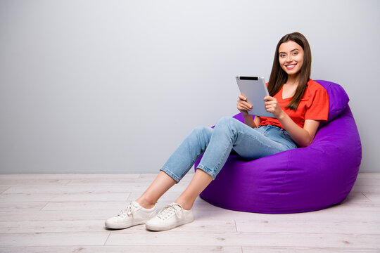 Portrait of her she nice attractive lovely cheerful cheery straight-haired girl sitting in bag chair using digital ebook device reading news recipe blog blogger light grey pastel color wall room