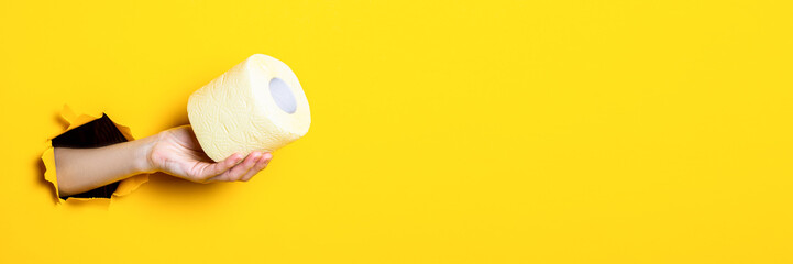 Woman's hand holds yellow toilet paper on torn yellow background. Banner.
