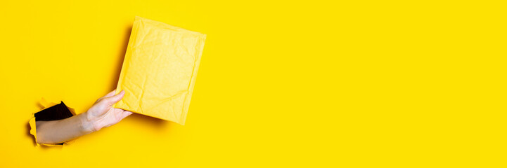 Female hand holds a yellow mail envelope on a torn yellow background. Banner. - obrazy, fototapety, plakaty