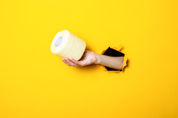 Woman's hand holds yellow toilet paper on torn yellow background