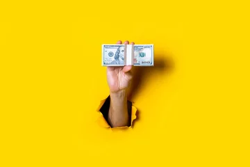 Fotobehang Female hand holds horizontally a bundle of money bills on a yellow background. © Alex