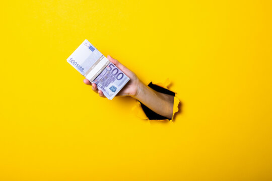 Woman's hand holds a bundle of five hundred euro bills on a yellow background.
