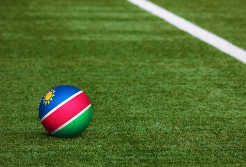 Fototapeta na wymiar Namibia flag on ball at soccer field background. National football theme on green grass. Sports competition concept.
