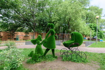 Flower sculpture of green grass of woman with a pram and girl. Topiary.