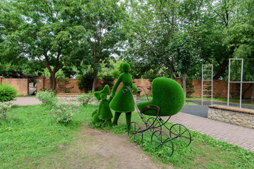 Flower sculpture of green grass of woman with a pram and girl. Topiary.