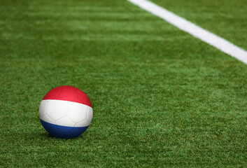 Fototapeta na wymiar Netherlands flag on ball at soccer field background. National football theme on green grass. Sports competition concept.