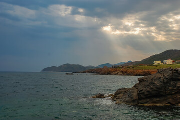 The sun's rays break through the clouds over the sea, sunset, coast, mountains in the haze