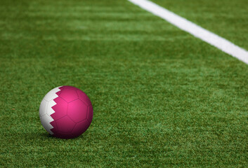 Fototapeta na wymiar Qatar flag on ball at soccer field background. National football theme on green grass. Sports competition concept.