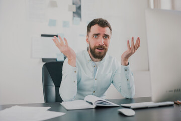 Fototapeta premium young bearded brunette man looking desperate while working on business project in his modern office, holding his hands in the air, work routine concept