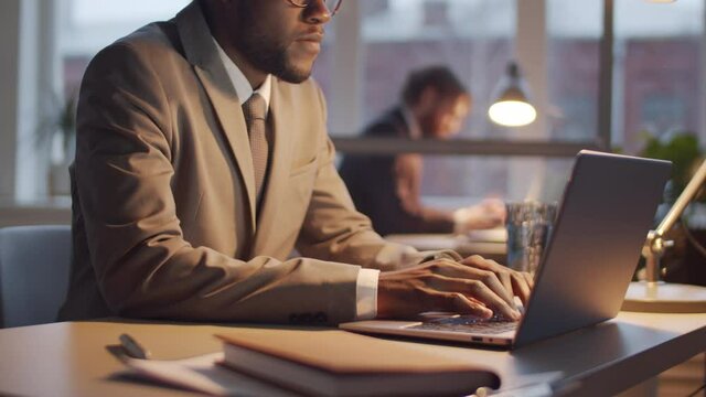 Midsection shot of afro-american businessman in formalwear working on laptop at office desk in the evening