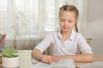 Schoolgirl studying at home. Young girl reading book at the table. Distance education, home education. Self isolation concept