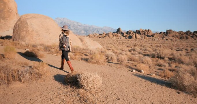Young woman is hiking in desert rocky park in summer on sunrise. Active healthy Caucasian woman with a backpack exploring in outdoors. Female traveler walks along nature park with motion background.