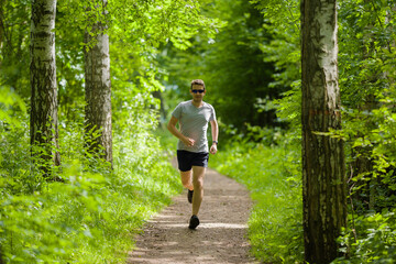 One young, adult man running in green forest on natural trail in sunny summer day. Daily active...