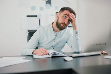young bearded brunette man looking tired and exhausted while working on business project in his...