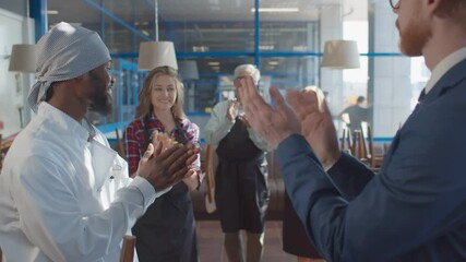 Close up of cafe owner shaking hands and congratulating african chef with promotion