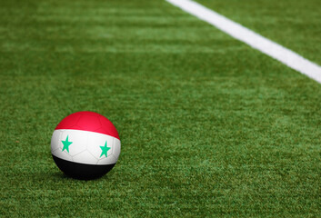 Syria flag on ball at soccer field background. National football theme on green grass. Sports competition concept.