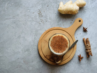 Indian drink masala tea with milk and spices on a wooden stand. The background is gray. Image with copy space, top view, horizontal orientation.