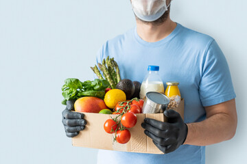 Safe food delivery concept - delivery man holds gloceries wearing medical mask and gloves