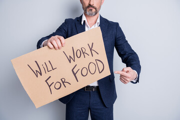 Cropped photo of serious poor homeless dismissed guy suffer financial crisis lost work job hold placard search work for food exchange direct finger card wear suit isolated grey background