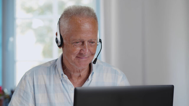 Senior Man In Headset With Laptop Having Video Chat Sit At Home