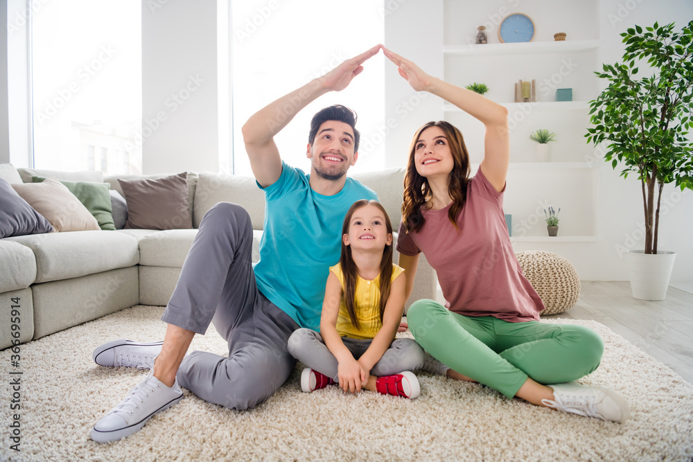 Poster Full length photo of positive three people daddy mommy small kid sit carpet floor make hands roof enjoy cozy insurance house indoors