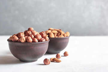 Obraz na płótnie Canvas Nuts in clay bowls on a gray background with a copy space. Hazelnuts and almonds